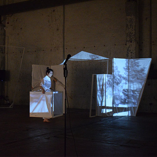 Performer Wei Zhang is walking with a set element while a projection is mapped on top of the element